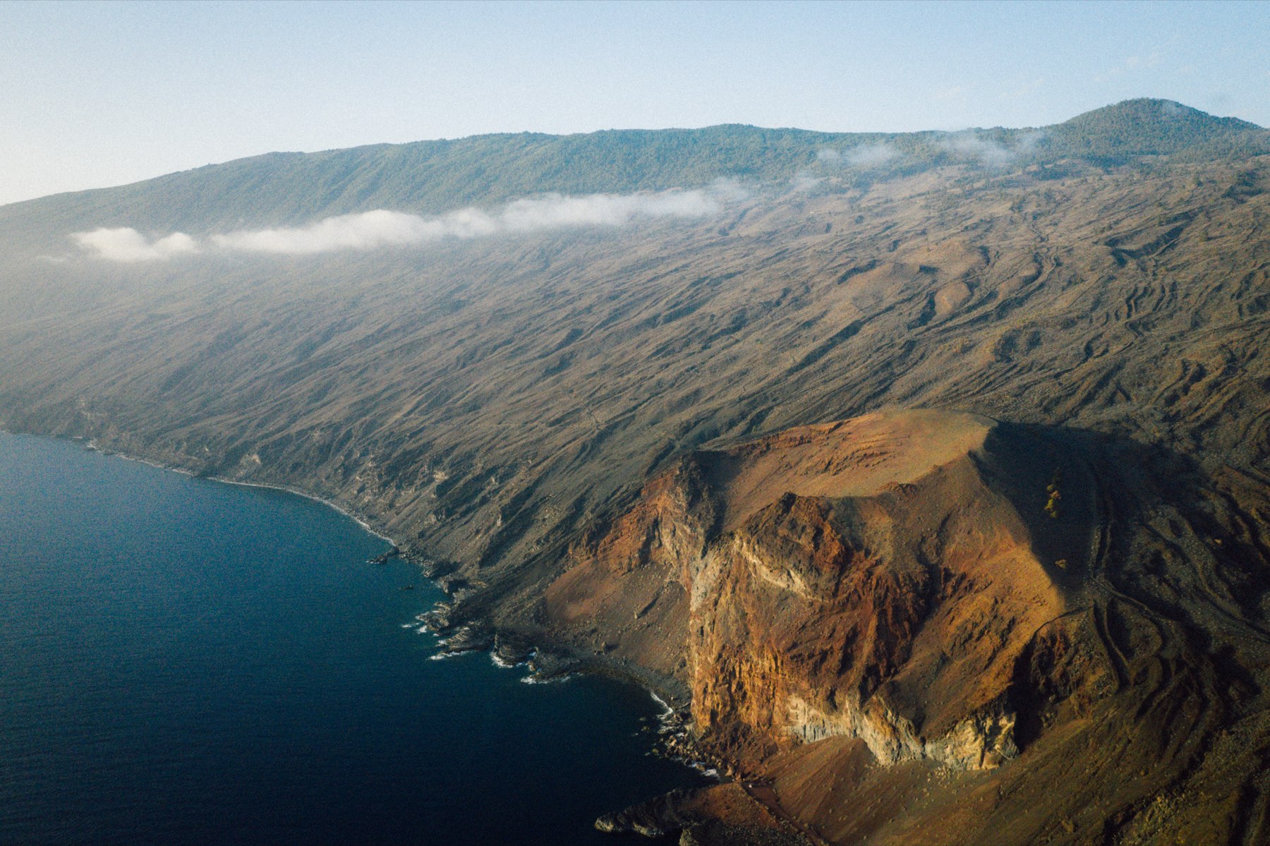 Aerial view of a long volcanic coastline under a band of cloud