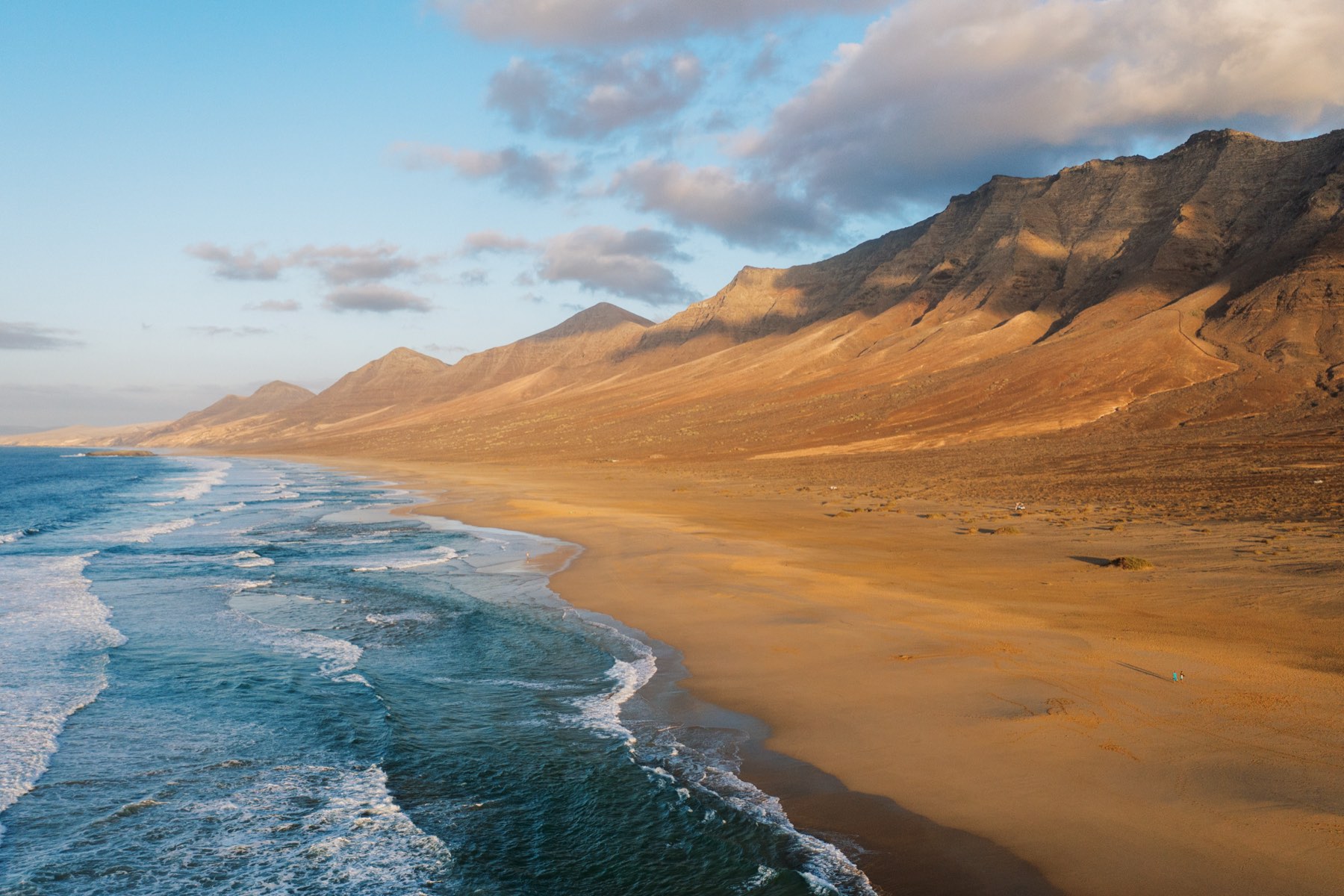 Long empty beach below a mountain ridge, waves rolling in