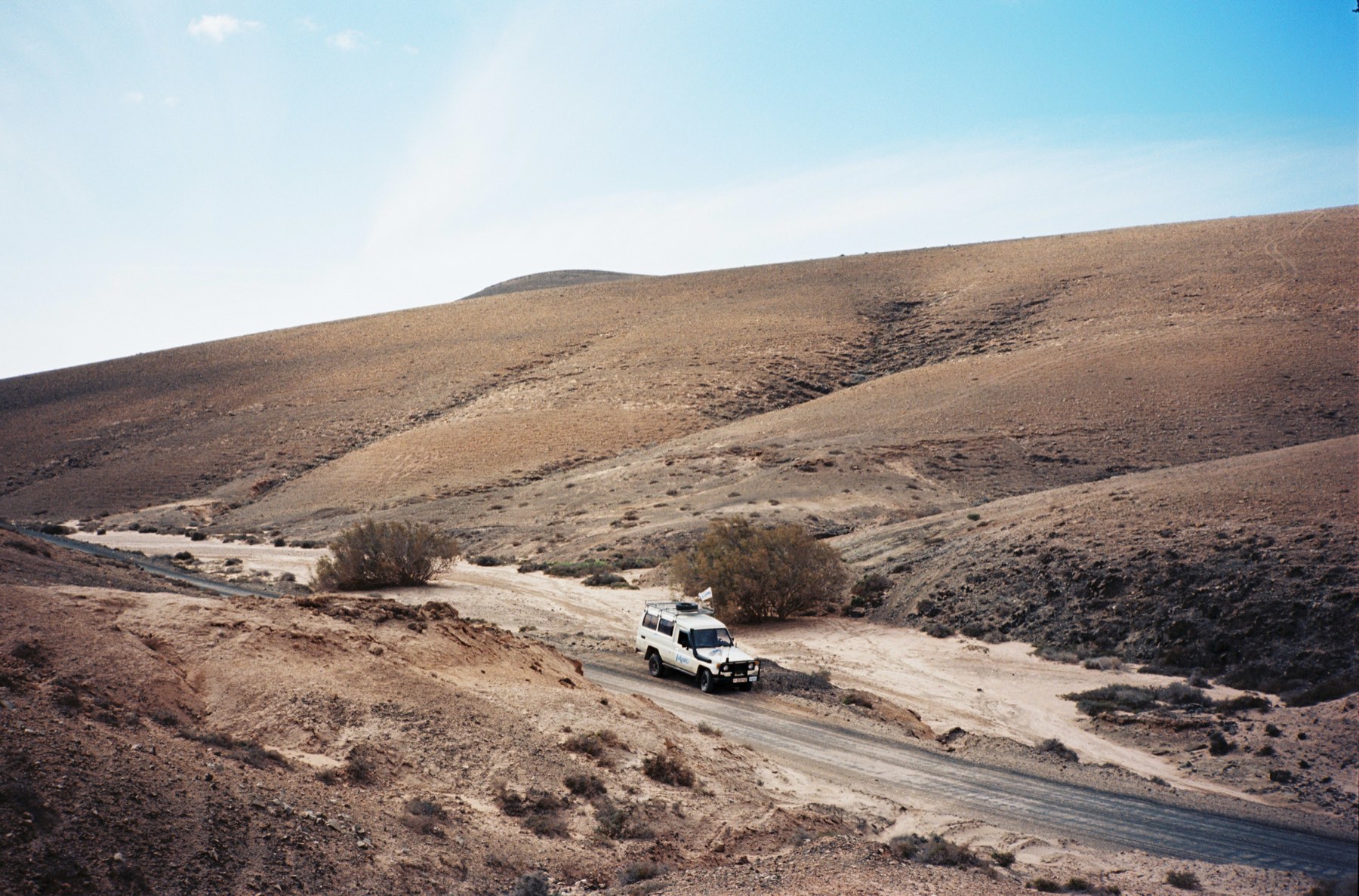 A white off-road car on a dirt track through bare hills
