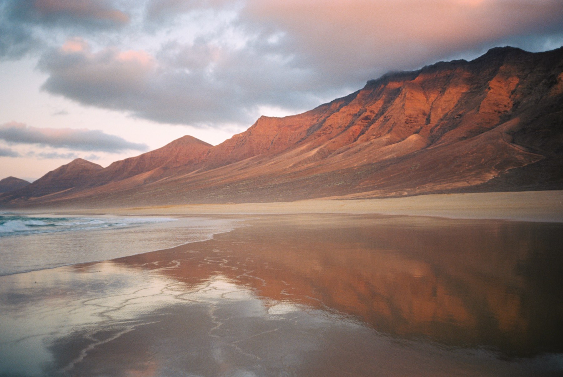 Red mountains mirrored on wet sand at sunset